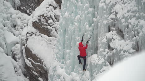 ice climber climbing on frozen waterfall in cold white winter mountain landscape