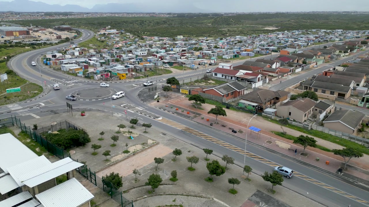 Auto attraversano una rotonda ai margini della township di Langa, dividendo baracche informali da abitazioni formali sotto una luce diurna nuvolosa