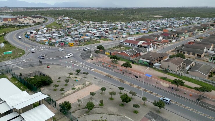 Auto attraversano una rotonda ai margini della township di Langa, dividendo baracche informali da abitazioni formali sotto una luce diurna nuvolosa