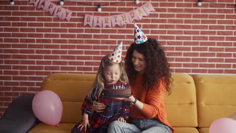 Mother-holding-in-hands-small-birthday-cake-while-daughter-blowing-out-the-candles