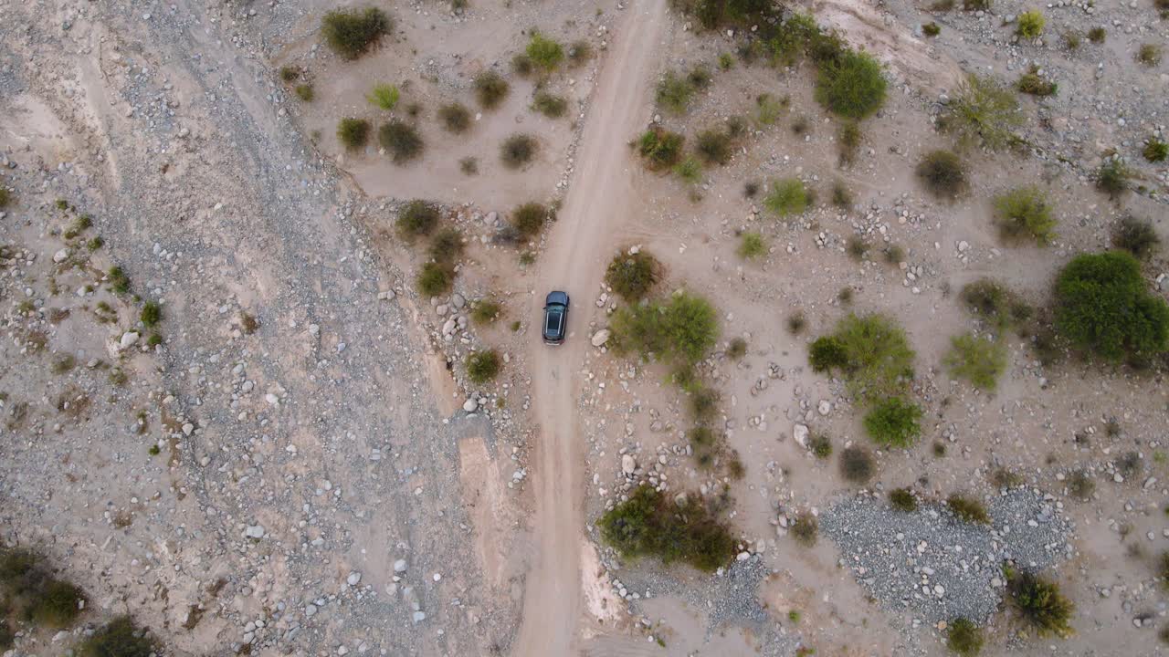 Ripresa aerea con drone dall'alto che segue un'auto grigia che percorre una strada sterrata attraverso il deserto di Tatón a Catamarca, Argentina.