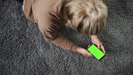 overhead shot of woman looking at green screen with copy space on mobile phone lying on carpet