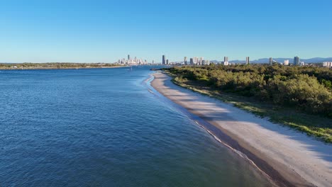 drone footage captures the serene gold coast seaway with sandy shores and city skyline under clear blue skies