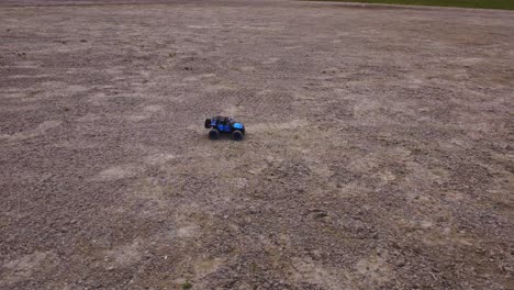 miniature 4x4 truck races over rough terrain, watched by a drone from an aerial high angle view