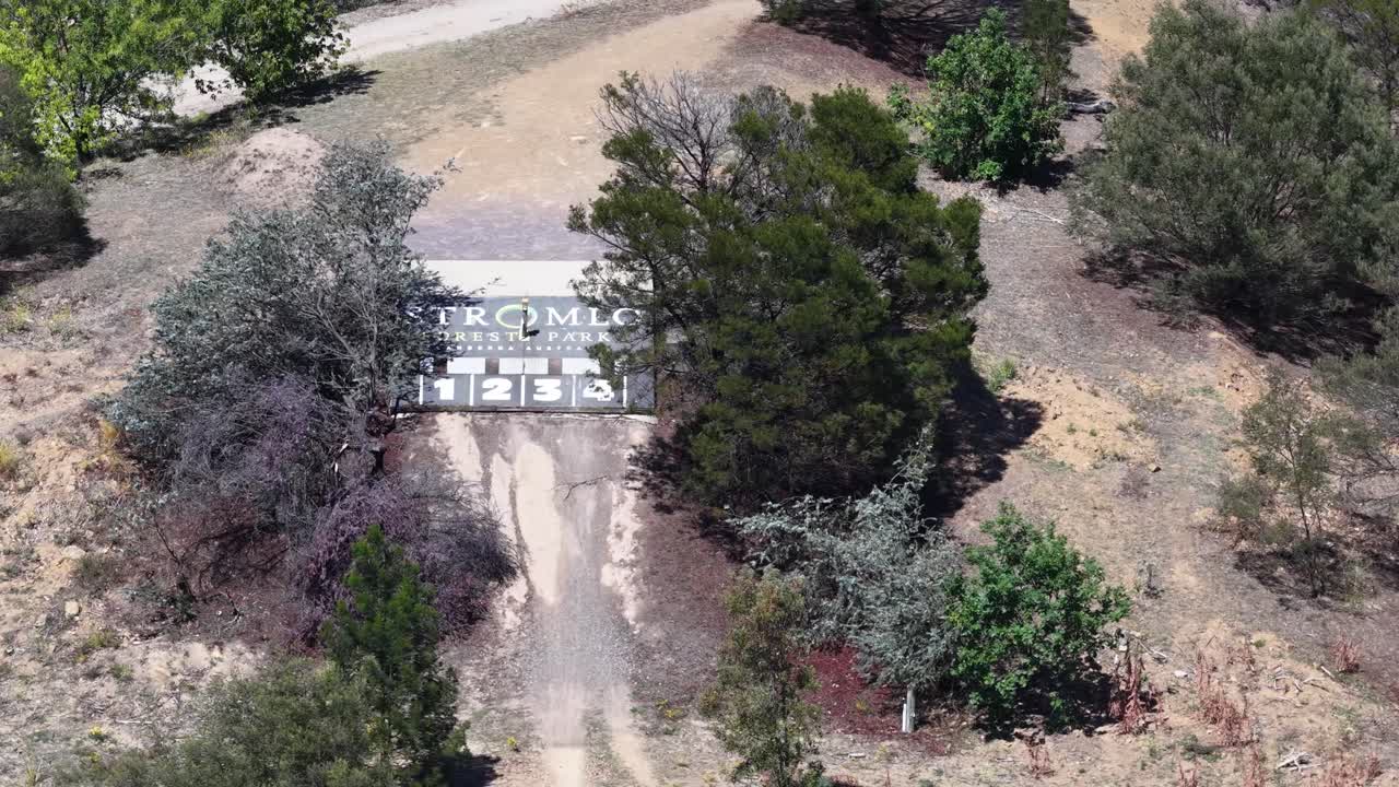 High angle drone shot reveals the entrance sign and surrounding bushland in bright daylight