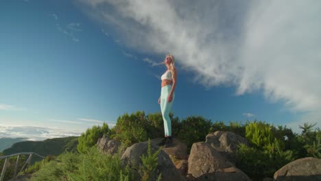 confident blond woman in sportswear standing on rock on summit enjoying sunrise, freedom moment