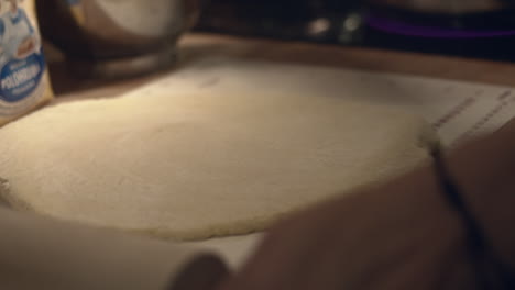 hand spreads flour and cuts dough with spatula in kitchen, close-up