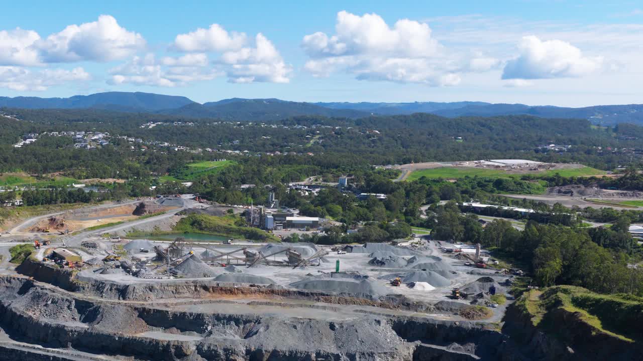 Drone footage captures a vast quarry landscape under clear skies, highlighting industrial activity and surrounding greenery