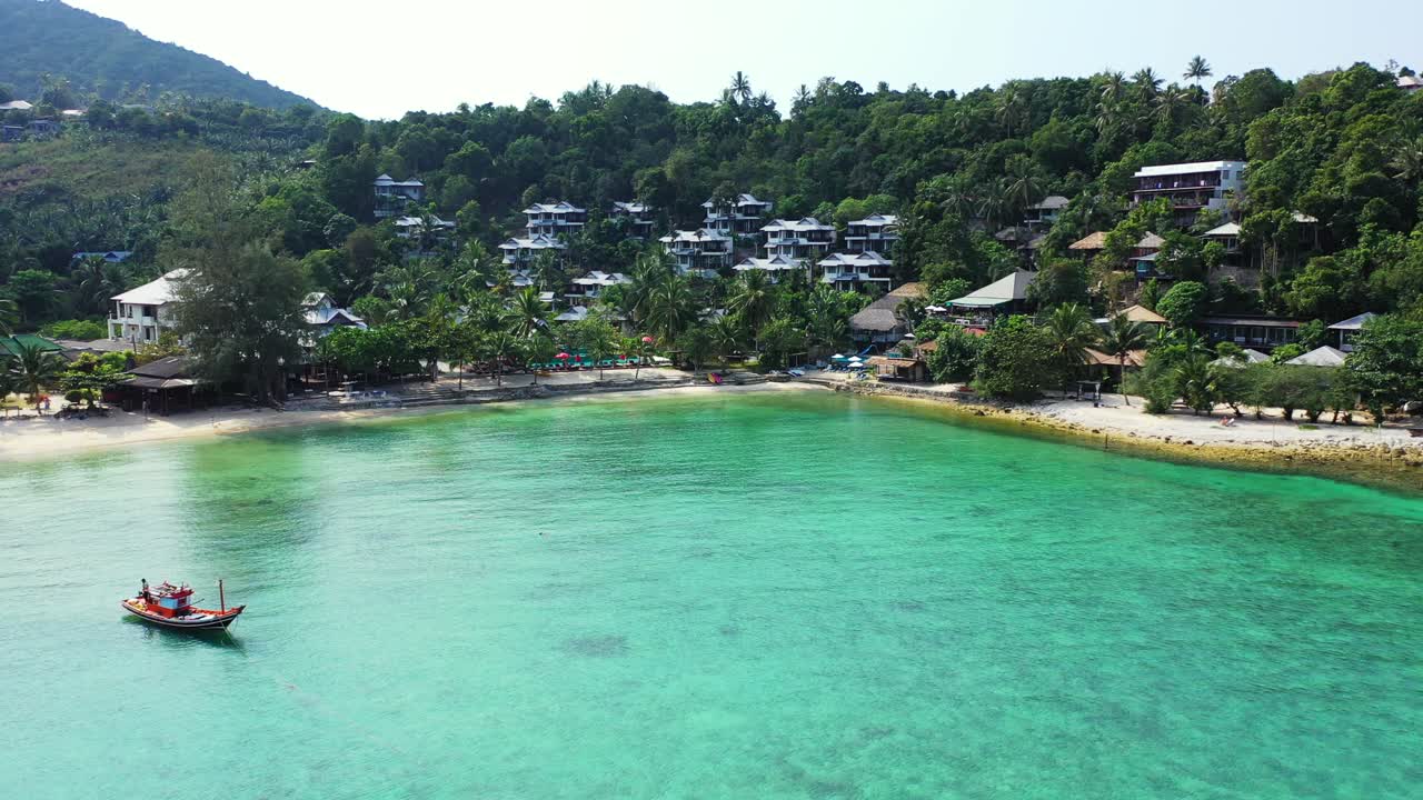 Traditional decorated fishing boat sailing slowly on calm turquoise lagoon of tropical island with sandy beach in front of holiday resort in Phangan, Thailand