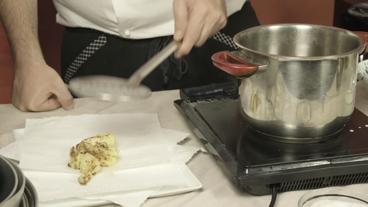 Close up chef's hands cook boiled cauliflowers from the pot adding salt to them