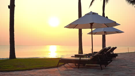 a pink and yellow ocean sunset lights up the beach and the empty sun lounges