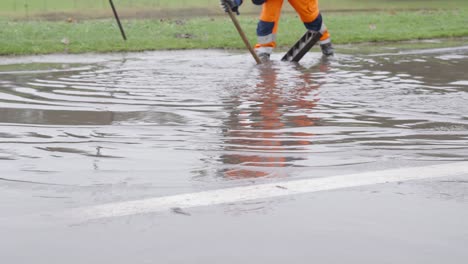 Trabajadores-De-La-Calle-De-La-Ciudad-Destapando-El-Drenaje-De-Alcantarilla-Para-Drenar-El-Agua-De-La-Inundación