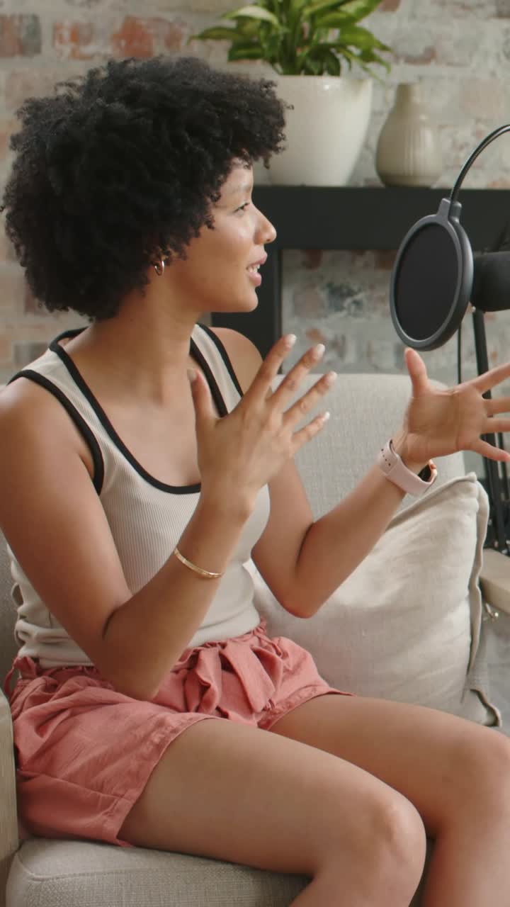 Vertical video: Recording starting, woman in tank leaning toward mic on sofa, gesturing for podcast