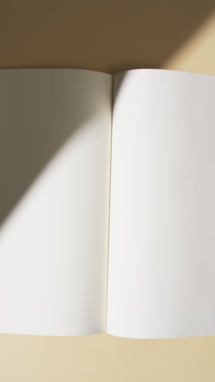 Vertical video of shadow over book with blank pages and copy space on yellow background