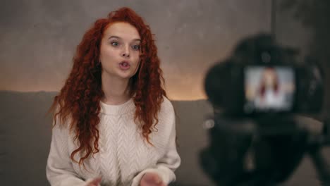 portrait of redhead young girl vlogger is talking in front of camera recording video for online blog for her followers