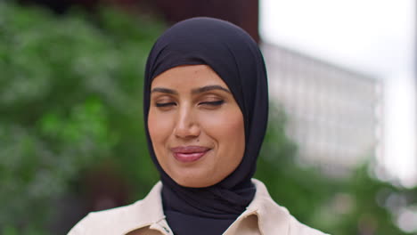 close up portrait of smiling muslim businesswoman wearing hijab with business suit outside modern office buildings 2