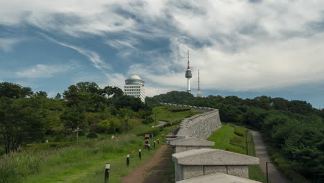 서울 성벽 과 남산 탑, 여름 날 에 고대 한국 요새 를 둘러보며 걸어가는 관광객 들 의 타임  ⁇ 스