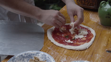 chef tops neapolitan pizza with fresh mozzarella cheese, on wooden table