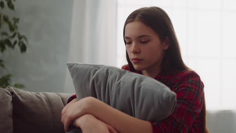 una joven triste se sienta abrazando una almohada en el sofá de la sala de estar