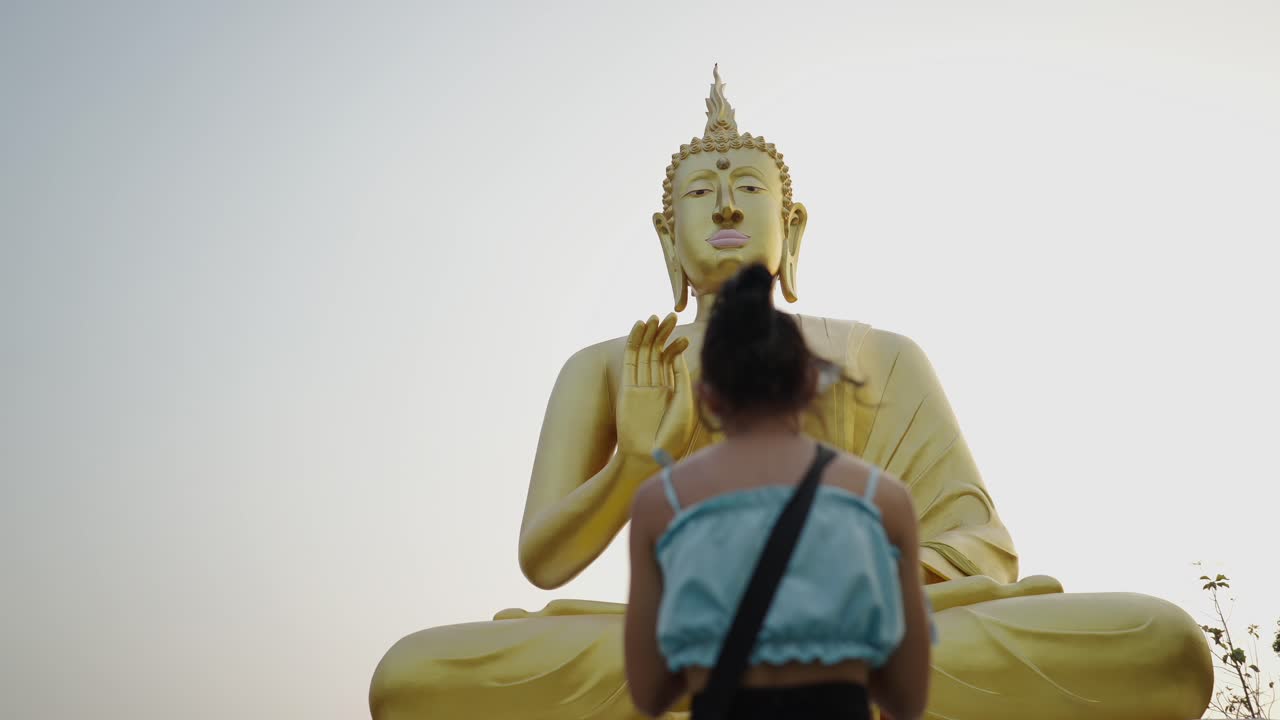 A woman praying before a large golden Buddha statue