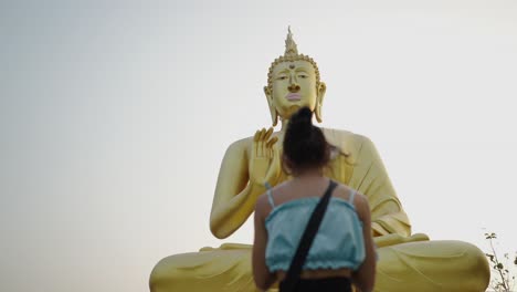 a woman praying before a large golden buddha statue