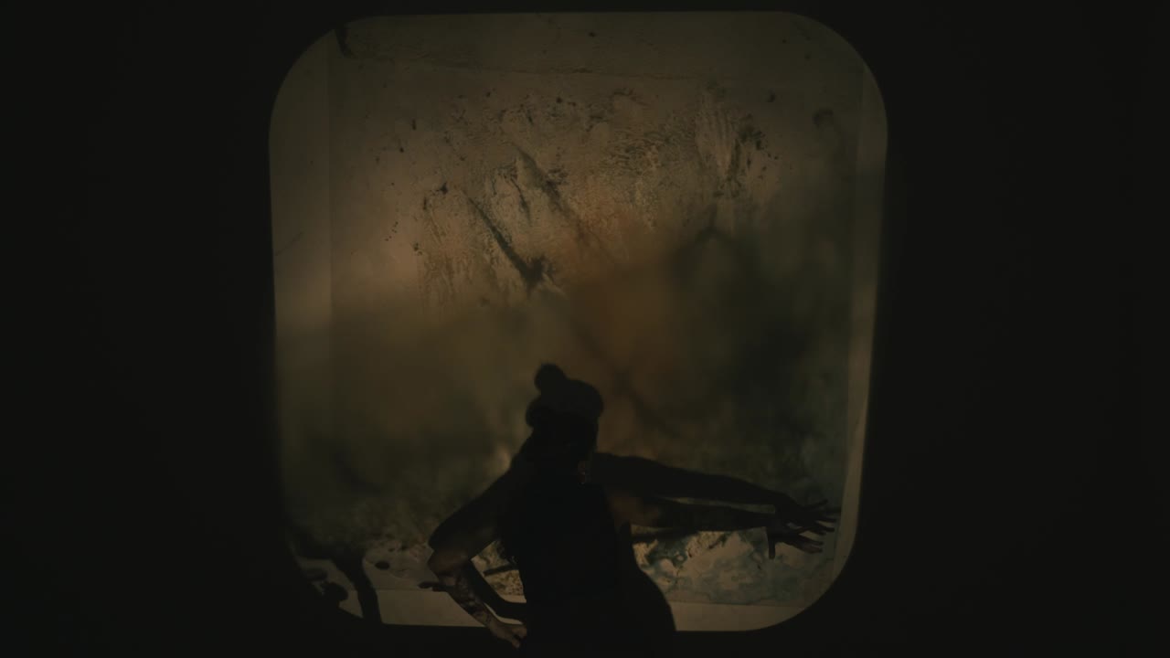 vista cercana de una mujer bailando y narrando una historia mientras otra persona cambia acetatos con luz suave, jugando con sombras