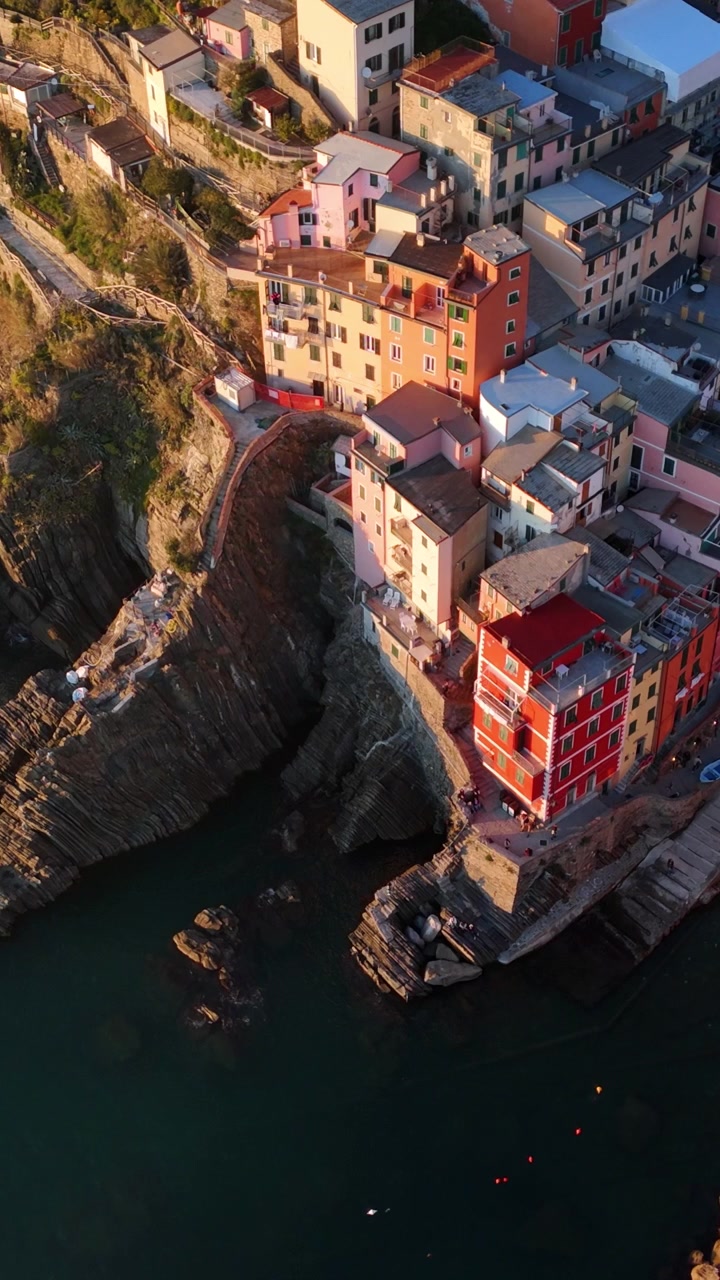 Un drone en vue plongeante survole les maisons colorées à flanc de falaise de Riomaggiore au coucher de soleil doré, aux Cinque Terre, en Italie