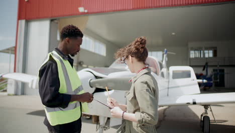 ground technician and inspector discussing aircraft in front of open hangar