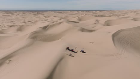 Fliegen-Sie-Durch-Schuss-Und-Enthüllen-Sie-ATV-Dünenbuggys,-Die-An-Einem-Sonnigen-Tag-In-Kalifornien-Durch-Sandige-Wüstengipfel-Fahren