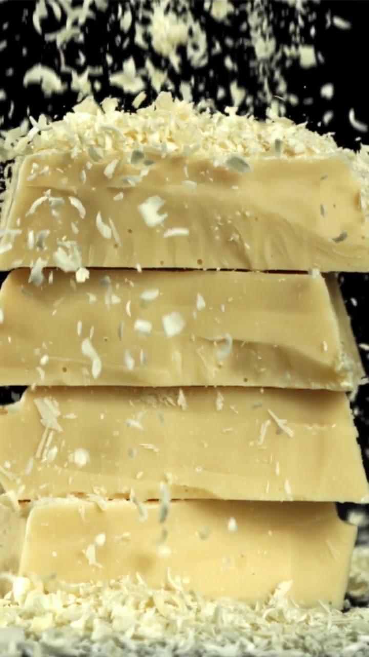 Scaglie di cioccolato bianco che cadono su tavolette di cioccolato impilate