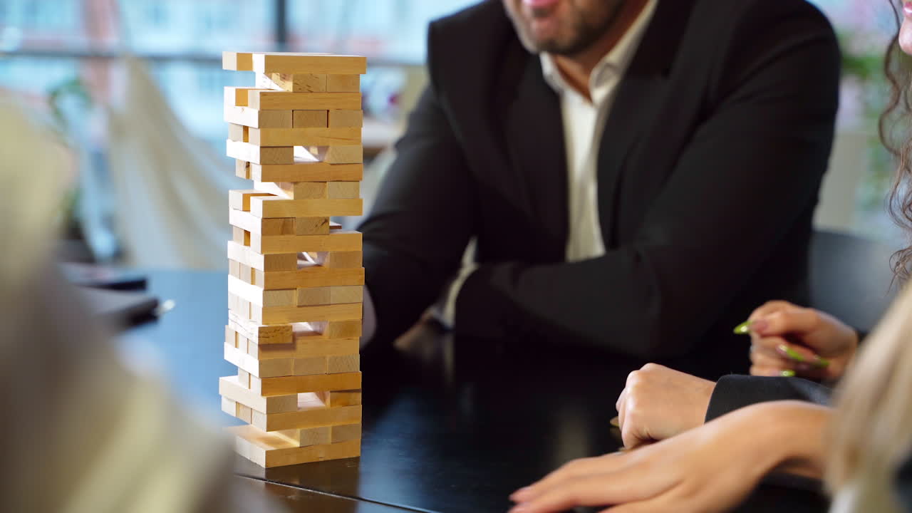 Bearded man in jacket pulls carefully jenga brick from a pile. People playing board games at leisure time.