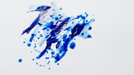 close up of blue paint shapes on white background with copy space, slow motion