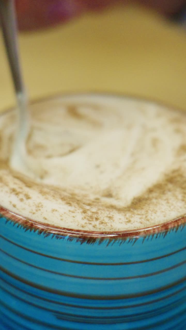 Bevanda cremosa con schiuma in una tazza a righe blu e una spolverata leggera di cacao in polvere sulla superficie, perfetta per viziarsi con prelibatezze e sorsi rinfrescanti