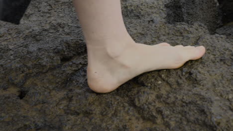Close-up of woman&#039;s feet walking on wet cliffs