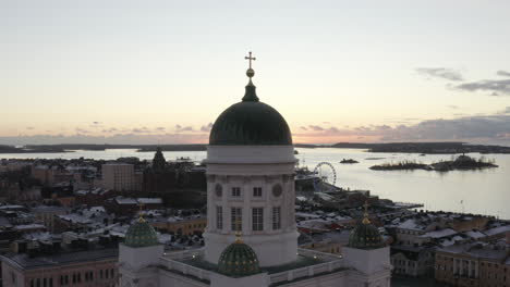 Vista-Aérea-De-Drones-De-La-Catedral-De-Helsinki-Con-El-Mar-Y-La-Puesta-De-Sol-En-El-Fondo