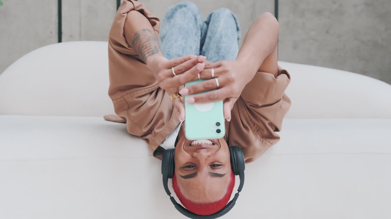 Young carefree cheerful african american woman lies upside down and holds phone