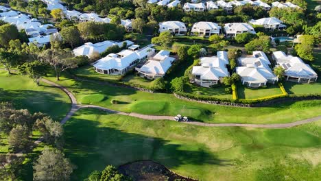 Drone footage captures a serene golf course with houses, trees, and a lake during golden hour