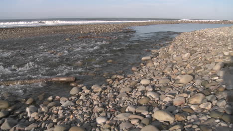 Wide-pan-of-water-flowing-out-of-the-Ventura-River-estuary-into-the-Pacific-Ocean-in-Ventura-California