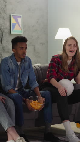 african-american man throws up chips in bowl watching football match with joyful friends at home slow motion. funny sports fans men and women rest