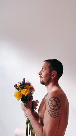 hombre sosteniendo flores con un tatuaje y una expresión pacífica