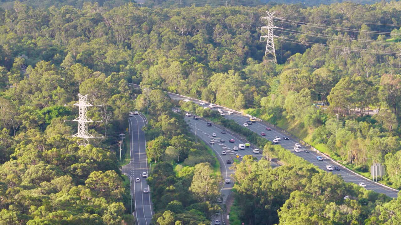 Drone captures traffic flow on a lush, tree-lined highway in Gold Coast, Australia, under bright daylight