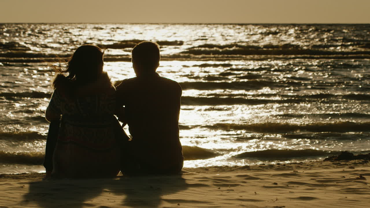 석양을 반영하는 바다의 배경에 앉아 사랑에 빠진 커플의 실루엣
