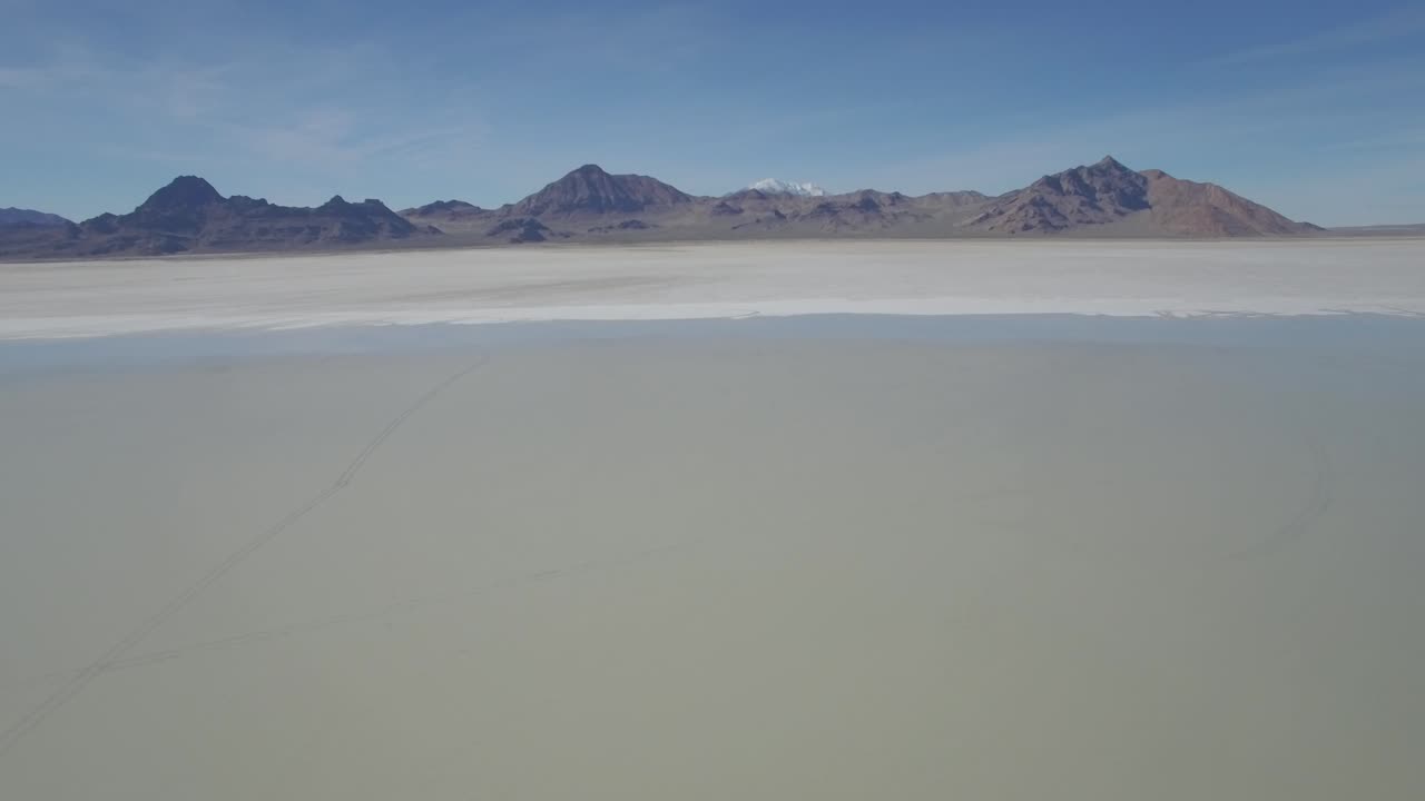 Aerial shot of salt flats moving upwards with a mountain range in view.