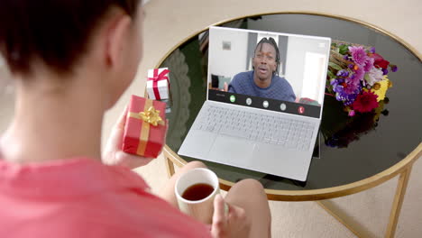 biracial woman holding gift and talking with biracial man talking on laptop screen