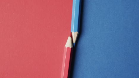 Overhead-view-of-blue-and-red-crayons-arranged-on-red-and-blue-background,-in-slow-motion