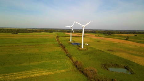 Drone-shot-of-two-working-wind-turbines-and-a-few-solar-panels-producing-green-electric-energy-on-a-cultivated-field-on-a-sunny-summer-day,-use-of-renewable-resources-of-energy,-parallax,-4k