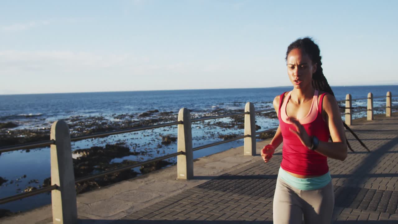 African american woman in sportswear running on promenade by the sea