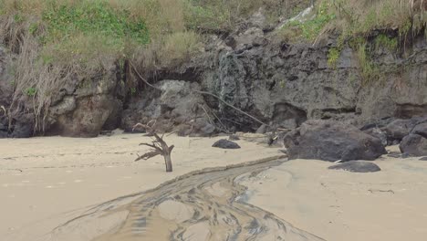 una pequeña cascada fluye de una duna de arena sobre una roca de playa negra y desemboca en el océano