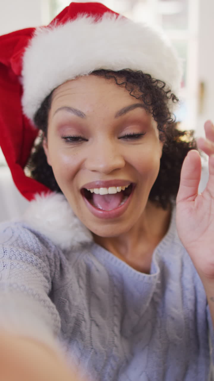video vertical del retrato de una feliz mujer afroamericana con el sombrero de santa haciendo una llamada de video