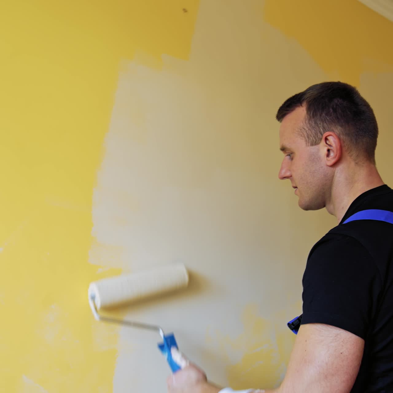 Professional young worker painting walls indoors. Paint roller in man's hands. Craftsman doing makeover in the room. Painting services